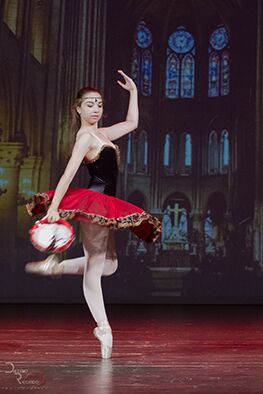 Ballerina in un elegante costume rosso e nero che danza sul palco, illuminata da uno sfondo di una cattedrale gotica, durante una performance a Viterbo.